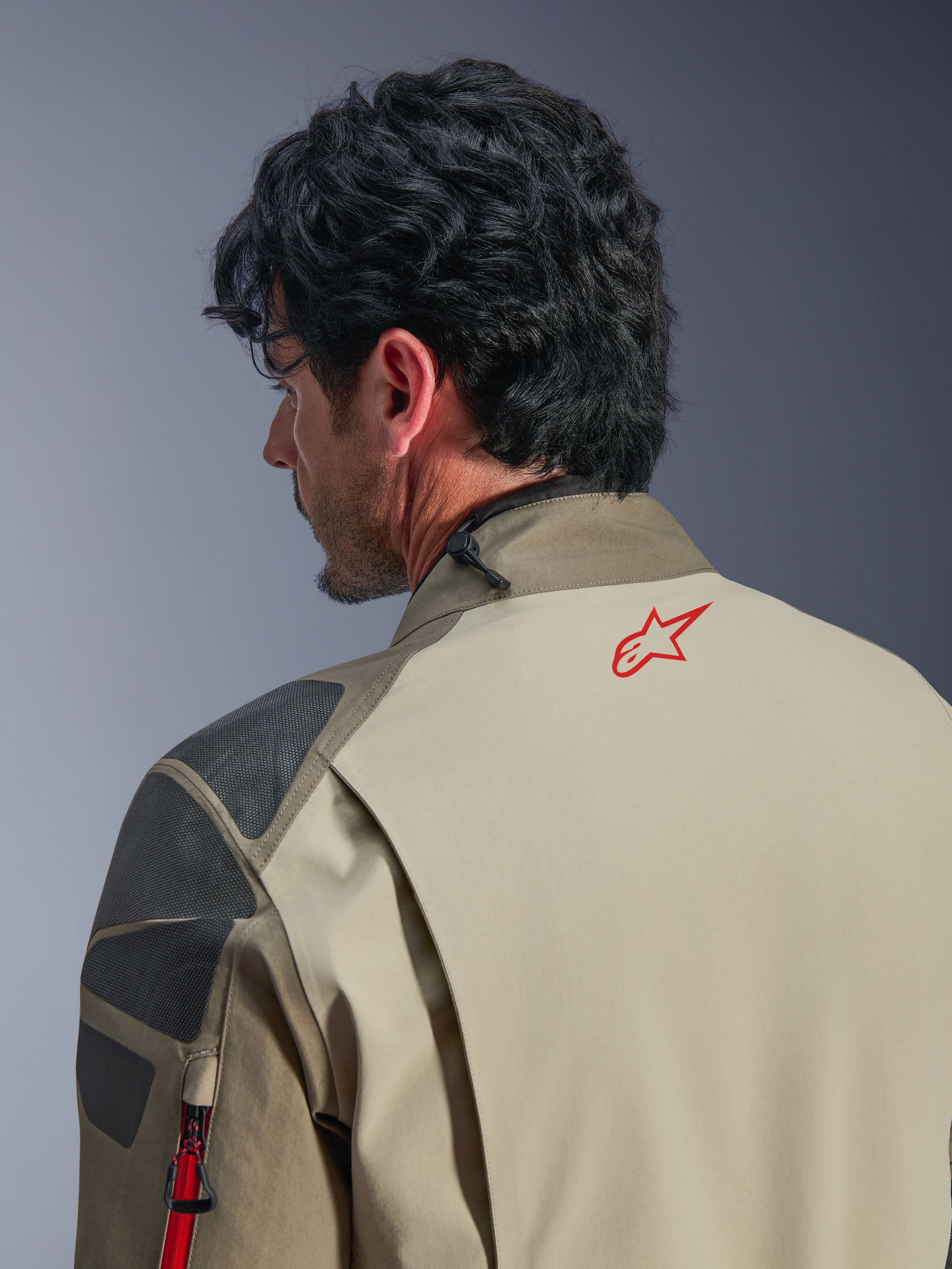 Chaqueta Alpinestars Nazca 3L GORE-TEX PRO, chaqueta de aventura en color Walnut Rock Brown, primer plano de la espalda y el hombro, logotipo de estrella roja en el cuello, paneles de refuerzo texturizados en gris, construcción textil duradera para conducción de motocicletas