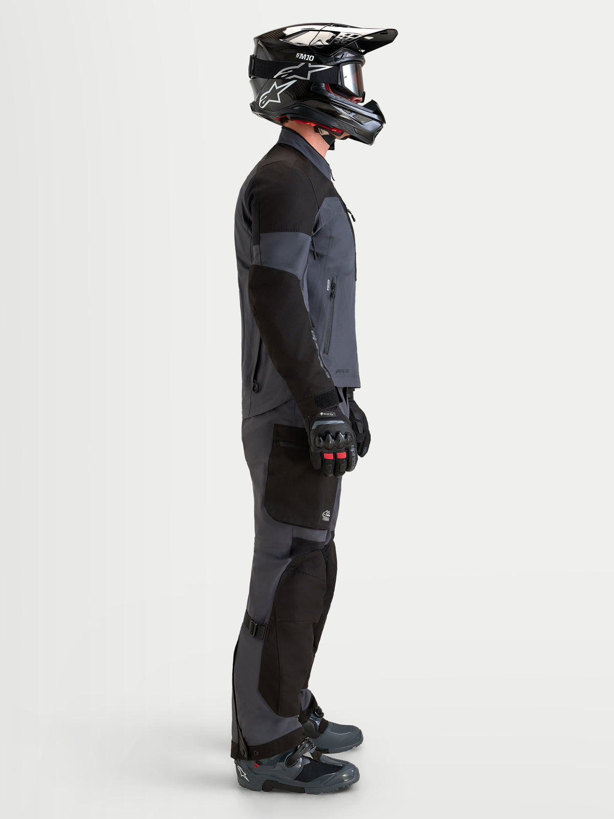 Alpinestars Arenis Gore-Tex Gear Set, men's adventure touring motorcycle jacket and pants in black and deep gray, side profile view on a model wearing matching helmet and boots, waterproof all-terrain riding apparel.