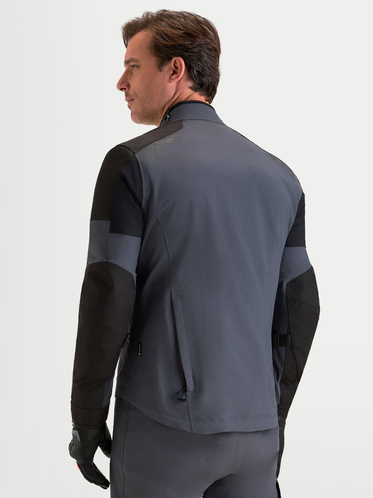 Alpinestars Arenis Gore-Tex Chaqueta, chaqueta de moto de aventura para hombre en negro y gris oscuro, vista del perfil trasero que muestra la construcción textil impermeable y el cuello ergonómico en modelo