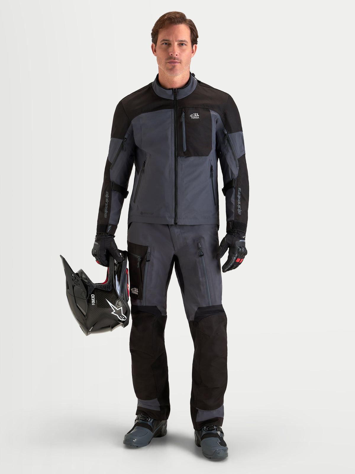 Alpinestars Arenis Gore-Tex Chaqueta, chaqueta de moto de aventura para hombre en negro y gris oscuro, usada por un piloto que sostiene un casco, mostrando la construcción textil GORE-TEX impermeable