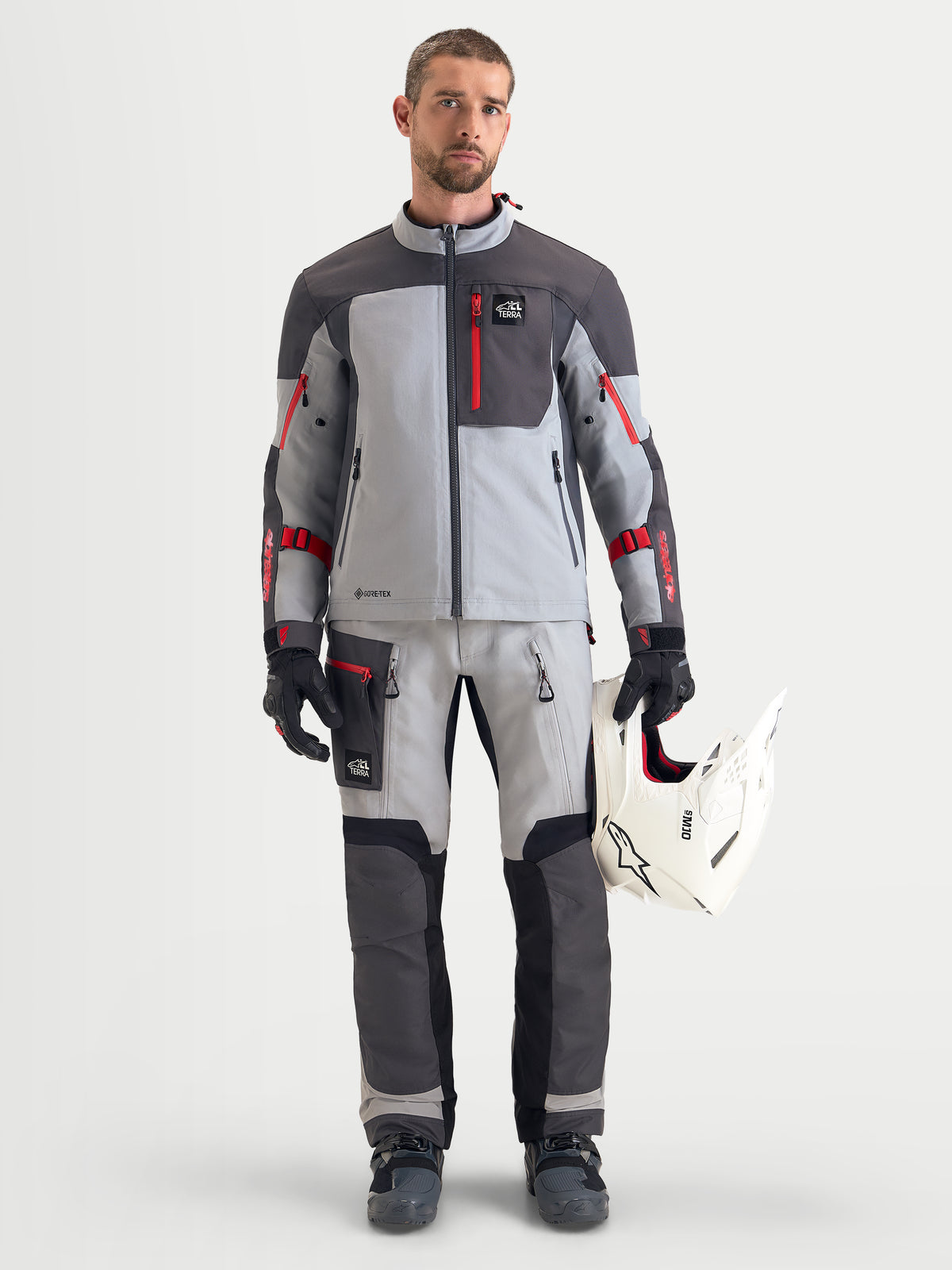 Alpinestars Arenis Gore-Tex Chaqueta, chaqueta de moto de aventura para hombre en gris medio, gris oscuro y negro, usada por un modelo que sostiene un casco blanco