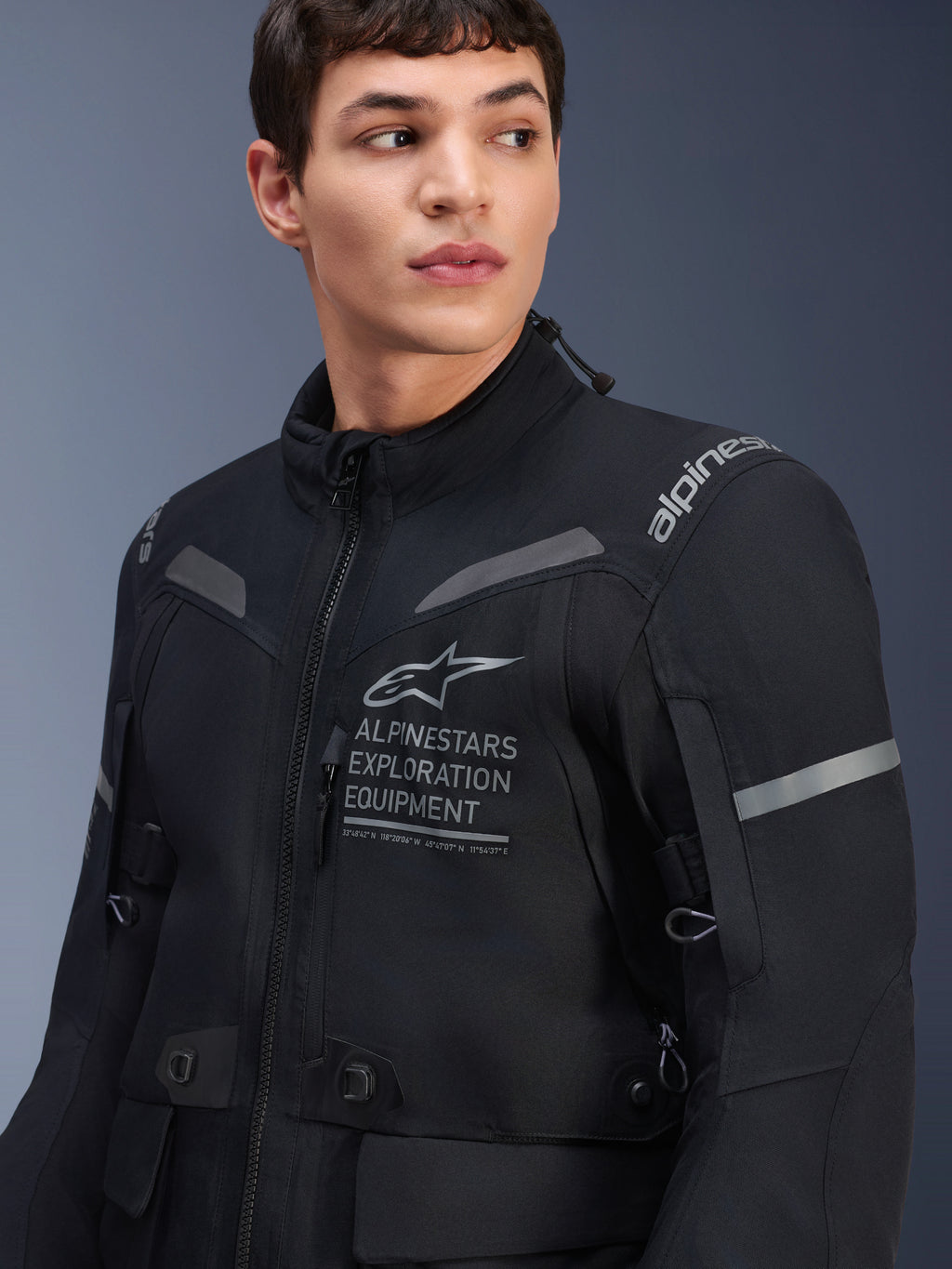 Chaqueta Alpinestars ST-7 2L GORE-TEX, chaqueta de moto, negro y gris oscuro, vestida por un modelo masculino, con el logotipo Alpinestars Exploration Equipment en el pecho, detalles grises reflectantes y construcción textil preparada para la aventura