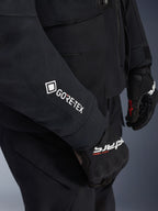 Chaqueta Alpinestars ST-7 2L GORE-TEX, negro y gris oscuro, primer plano de la manga con el logotipo de GORE-TEX en blanco, usada con guantes negros de conducción adventure, equipamiento de moto impermeable