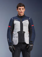 Alpinestars ST-7 2L GORE-TEX Jacket, Motorcycle Adventure Touring Jacket, Ice Gray and Dark Blue with Red accents, Waterproof and breathable, worn by a model with black gloves, featuring Alpinestars Exploration Equipment branding on the chest
