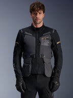 Alpinestars ST-7 2L GORE-TEX Jacket, Men's Adventure Touring Motorcycle Jacket, Deep Gray and Black with Khaki accents, featuring 'Alpinestars Exploration Equipment' branding, waterproof cargo pockets, and high collar, worn by a model with black gloves