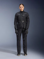 Female rider wearing Alpinestars Women Stella ST-7 2L GORE-TEX Jacket and Pants, Black motorcycle touring outfit, waterproof and breathable technical gear, worn with matching black gloves and boots, full-body protective gear with reflective elements, modern technical design for adventure riding