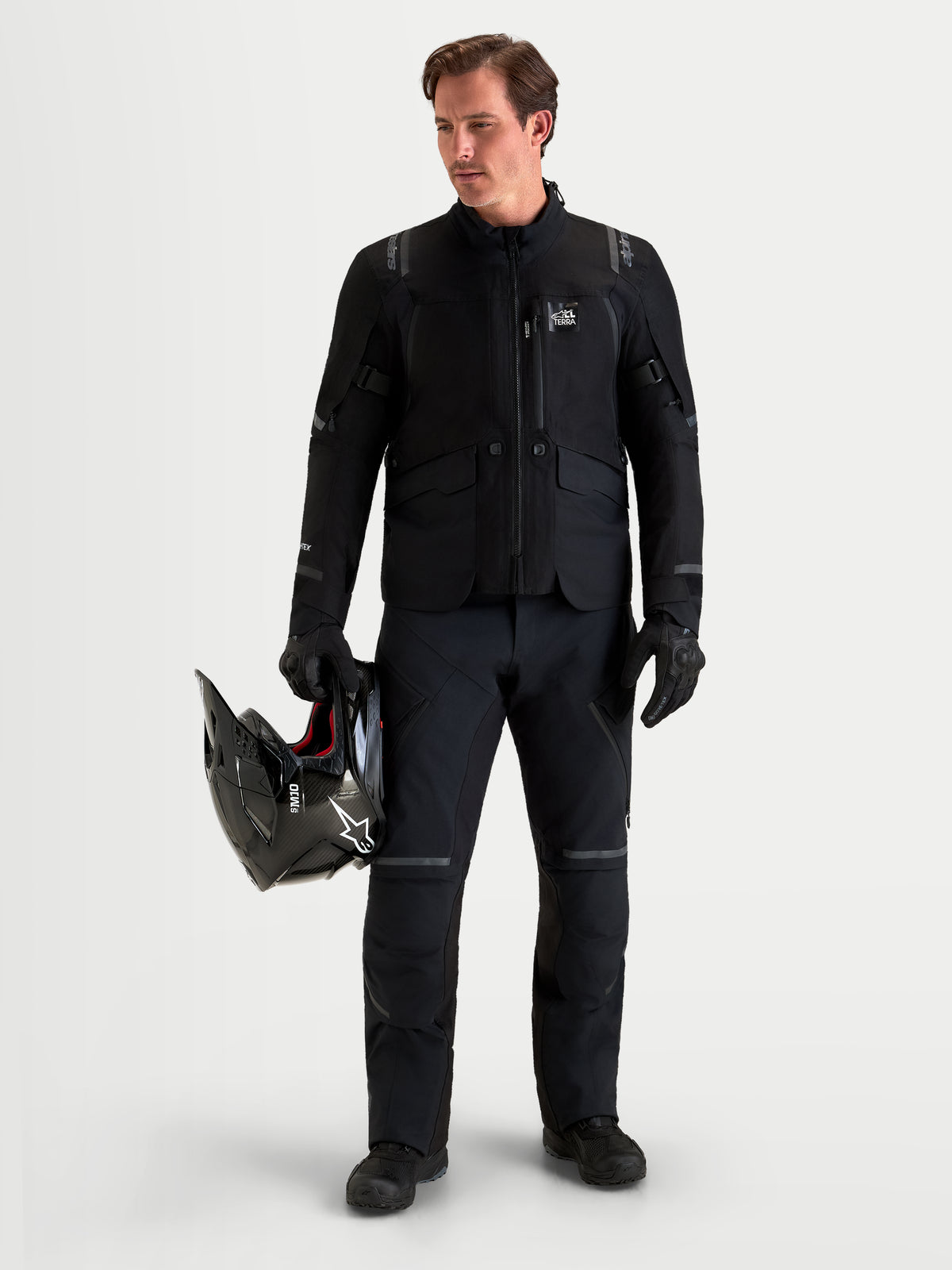 Alpinestars St-7 V2 2L Gore-Tex Pantalones Short, pantalones de moto de aventura para hombre, negros, vista frontal en modelo con equipamiento a juego y casco en mano, prendas impermeables para todo terreno con certificación AA.