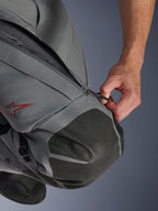 Pantalones Alpinestars Nazca 3L GORE-TEX PRO, pantalones de moto adventure, gris oscuro y negro, primer plano de una mano abriendo la entrada de ventilación con cremallera en el muslo, con refuerzos de rodilla en Superfabric texturizado y logotipo de estrella de Alpinestars en rojo, construcción textil técnica para protección en cualquier clima