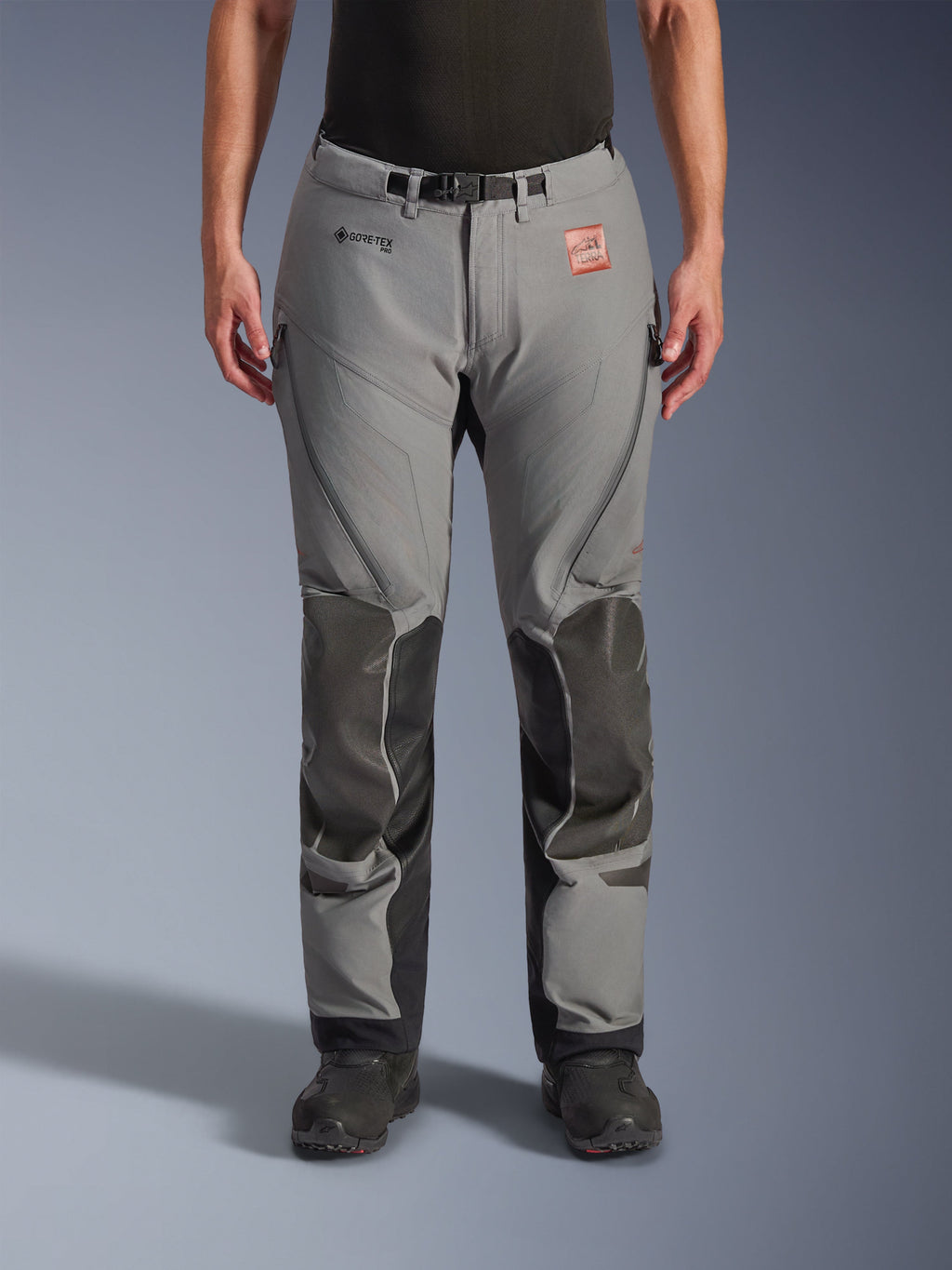Alpinestars Nazca 3L Gore-Tex Pro Pants - Short, pantalones de moto de aventura, gris oscuro y negro, vista frontal en modelo, con paneles reforzados en las rodillas, logotipo de GORE-TEX PRO y parche de cuero TERRA, construcción técnica impermeable de 3 capas para adventure touring