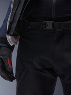 Pantalones Alpinestars ST-7 2L GORE-TEX, negros, primer plano de la cintura con cierre de hebilla magnética y construcción en tejido técnico duradero, usados con una chaqueta adventure touring a juego y guantes negros con logotipo rojo.