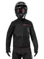 Chaqueta Alpinestars Pro-Dura, chaqueta de motociclismo off-road negra, vista frontal de un piloto con casco y gafas negros a juego, con logotipo de Alpinestars en rojo, bolsillos en el pecho con cremallera y construcción textil duradera para conducción de enduro.