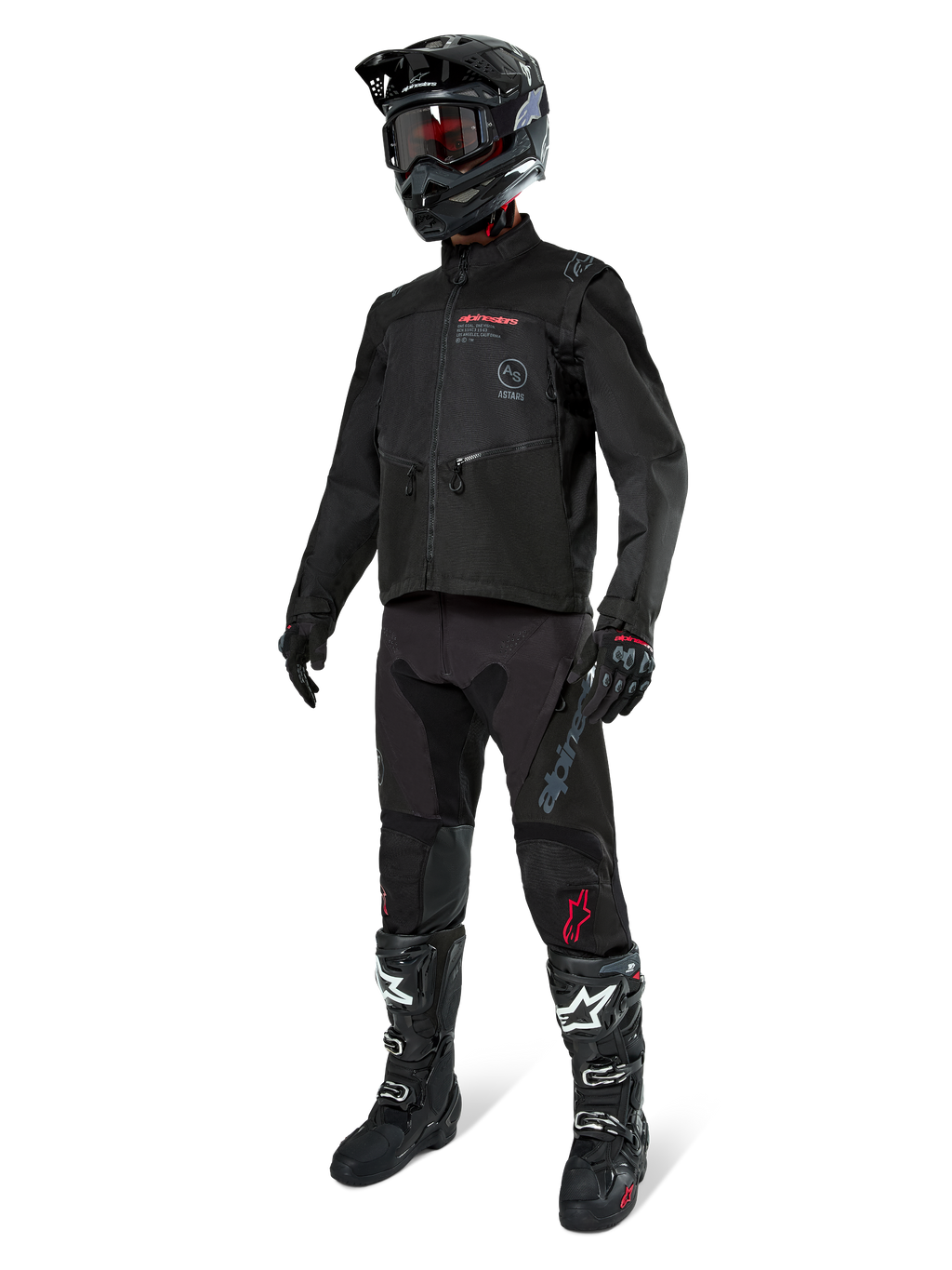 Piloto de motocross con equipamiento completo de carreras, chaqueta Alpinestars Pro-Dura en negro, pantalones negros con logotipos grises y detalles rojos, casco negro con gafas, y botas de motocross en blanco y negro, conjunto coordinado para enduro y conducción off-road