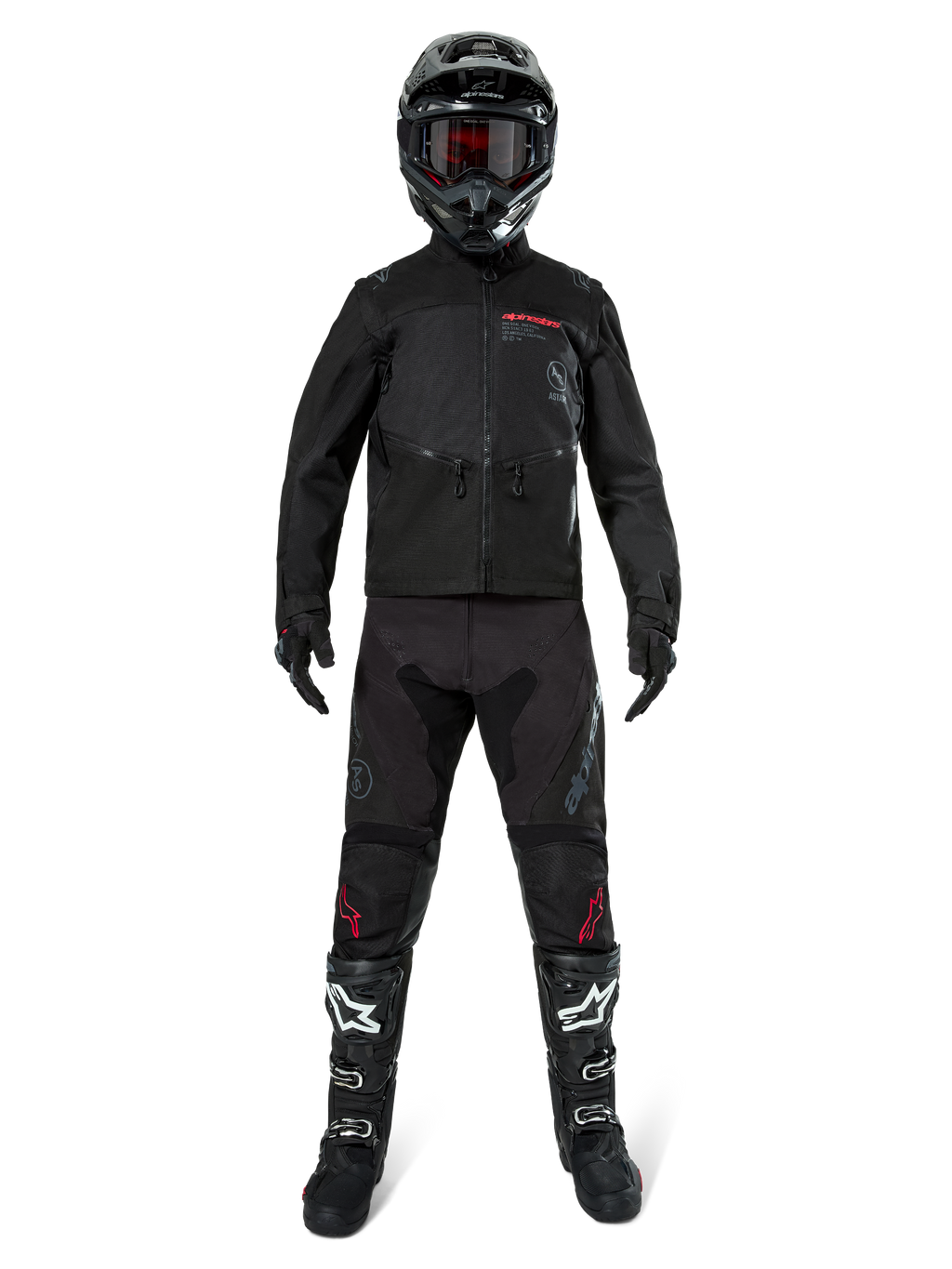 Chaqueta Alpinestars Pro-Dura, chaqueta de enduro off-road negra, mostrada en un modelo con un conjunto completo de equipamiento que incluye casco negro con gafas rojas, pantalones negros con detalles rojos, botas negras y blancas, y guantes negros, diseño robusto inspirado en el rally para recorridos por senderos