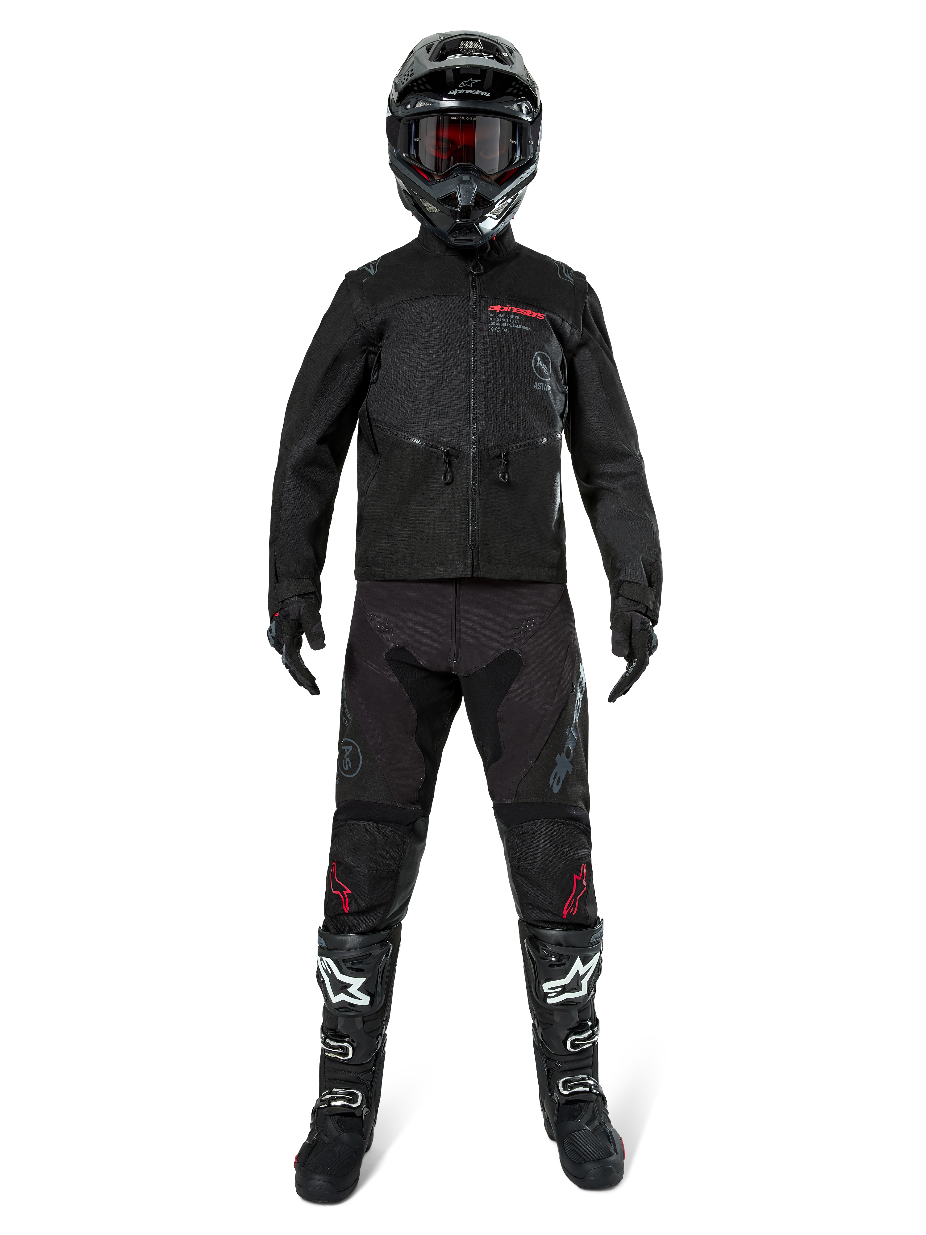 Chaqueta Alpinestars Pro-Dura, chaqueta de enduro off-road negra, mostrada en un modelo con un conjunto completo de equipamiento que incluye casco negro con gafas rojas, pantalones negros con detalles rojos, botas negras y blancas, y guantes negros, diseño robusto inspirado en el rally para recorridos por senderos