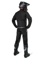 Chaqueta Alpinestars Pro-Dura, chaqueta de enduro off-road en color negro, vista trasera combinada con pantalones a juego y botas Tech 10 negras, con el logotipo de Alpinestars destacado en la parte inferior de la espalda, material textil robusto para conducción agresiva en senderos.
