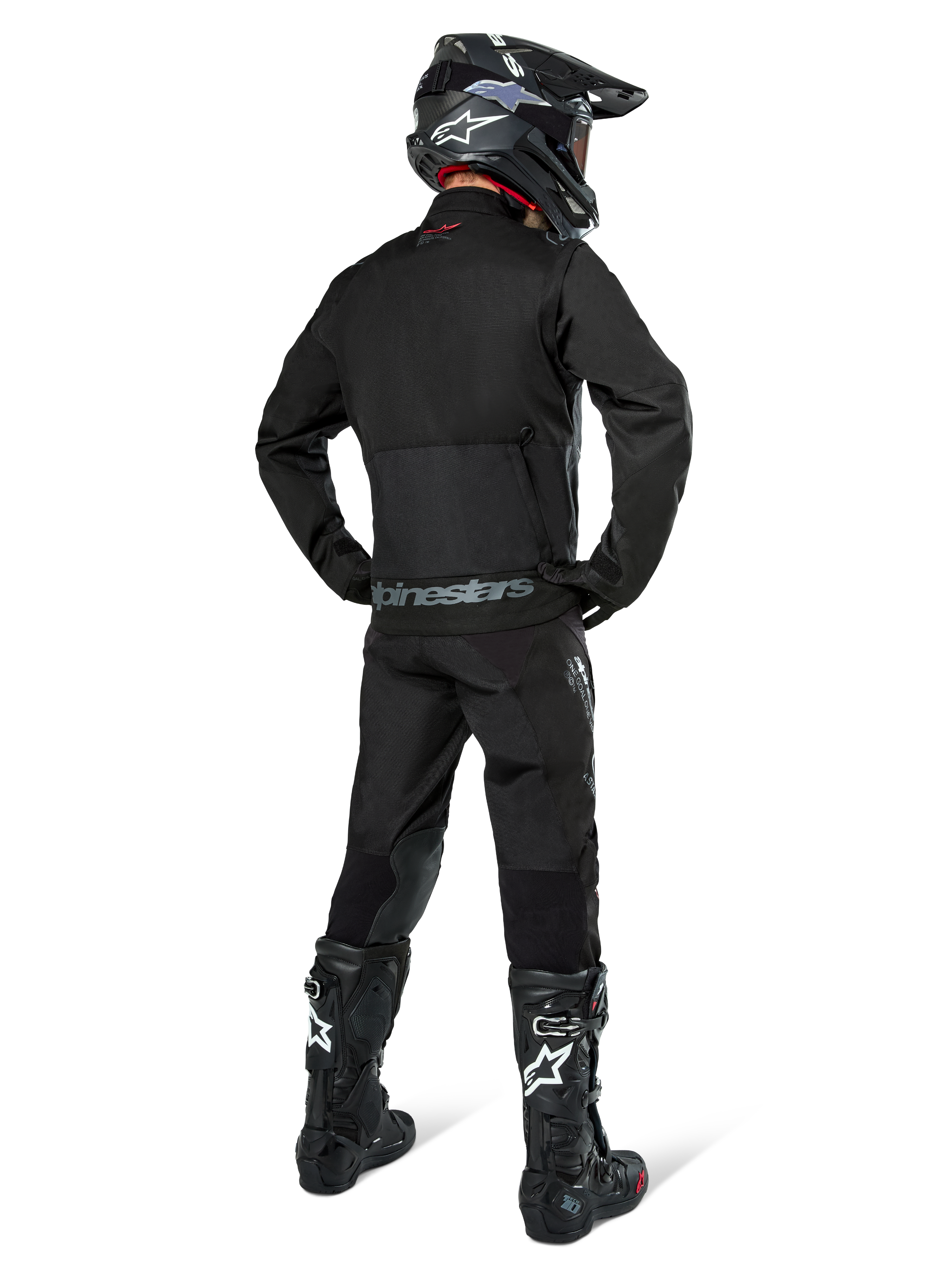 Chaqueta Alpinestars Pro-Dura, chaqueta de enduro off-road en color negro, vista trasera combinada con pantalones a juego y botas Tech 10 negras, con el logotipo de Alpinestars destacado en la parte inferior de la espalda, material textil robusto para conducción agresiva en senderos.
