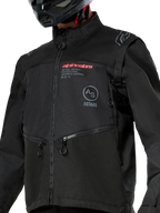 Chaqueta Alpinestars Pro-Dura, chaqueta de motociclismo off-road negra con el logotipo de Alpinestars en rojo y un logo circular Astars gris en el pecho, bolsillos con cremallera y confección en tejido ripstop resistente, diseño inspirado en el rally para la conducción de enduro.