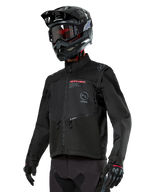 Chaqueta Alpinestars Pro-Dura, chaqueta de moto off-road, negra con logotipos rojos y grises, cuenta con bolsillos frontales con cremallera y cuello alto, usada con casco de motocross y guantes negros para carreras de enduro