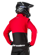 Chaqueta Alpinestars Pro-Dura, chaqueta de enduro off-road, roja y negra con logotipo de Alpinestars en blanco en el dobladillo trasero, vista desde atrás de un piloto con casco de motocross negro, diseño inspirado en el rally para conducción agresiva en senderos