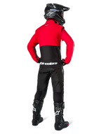 Piloto de motocross visto desde atrás vistiendo la chaqueta Alpinestars Pro-Dura en negro, rojo brillante y blanco, combinada con pantalones negros, casco negro y botas off-road negras, con una sección superior roja y una inferior negra con la marca Alpinestars en blanco en la espalda.
