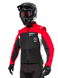 Chaqueta Alpinestars Pro-Dura, chaqueta de moto para enduro y off-road, negra con bloques de color rojo brillante y blanco, usada por un piloto con casco negro y gafas, con bolsillos delanteros con cremallera y logotipos de Alpinestars, construcción textil duradera para conducción en senderos