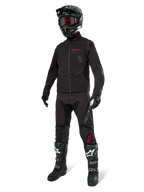 Chaqueta Alpinestars Lite-Dura Softshell, negra, mostrada en un maniquí como parte de un conjunto completo de equipamiento off-road que incluye pantalones negros, botas negras y blancas, casco negro con gafas rojas, ropa profesional de motocross y enduro.