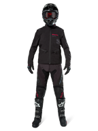 Piloto de motocross con la chaqueta Alpinestars Lite-Dura Softshell en negro con detalles rojos del logo, combinada con pantalones off-road negros a juego, casco negro y botas blancas y negras, equipamiento profesional completo de carreras de enduro.
