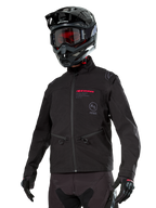 Alpinestars Lite-Dura Softshell Jacket, chaqueta de moto off-road negra con marca en rojo y logotipo AS, usada con casco de motocross negro, gafas rojas y guantes negros, con bolsillos con cremallera y puños ajustables, diseñada para enduro.