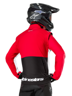 Alpinestars Lite-Dura Softshell Jacket, negro, rojo brillante y blanco, vista trasera en un piloto de motocross, parte superior del cuerpo y mangas en rojo con panel inferior trasero negro, bolsillo de almacenamiento trasero con cremallera, logotipo blanco de Alpinestars en el dobladillo inferior, usada con casco y pantalones negros