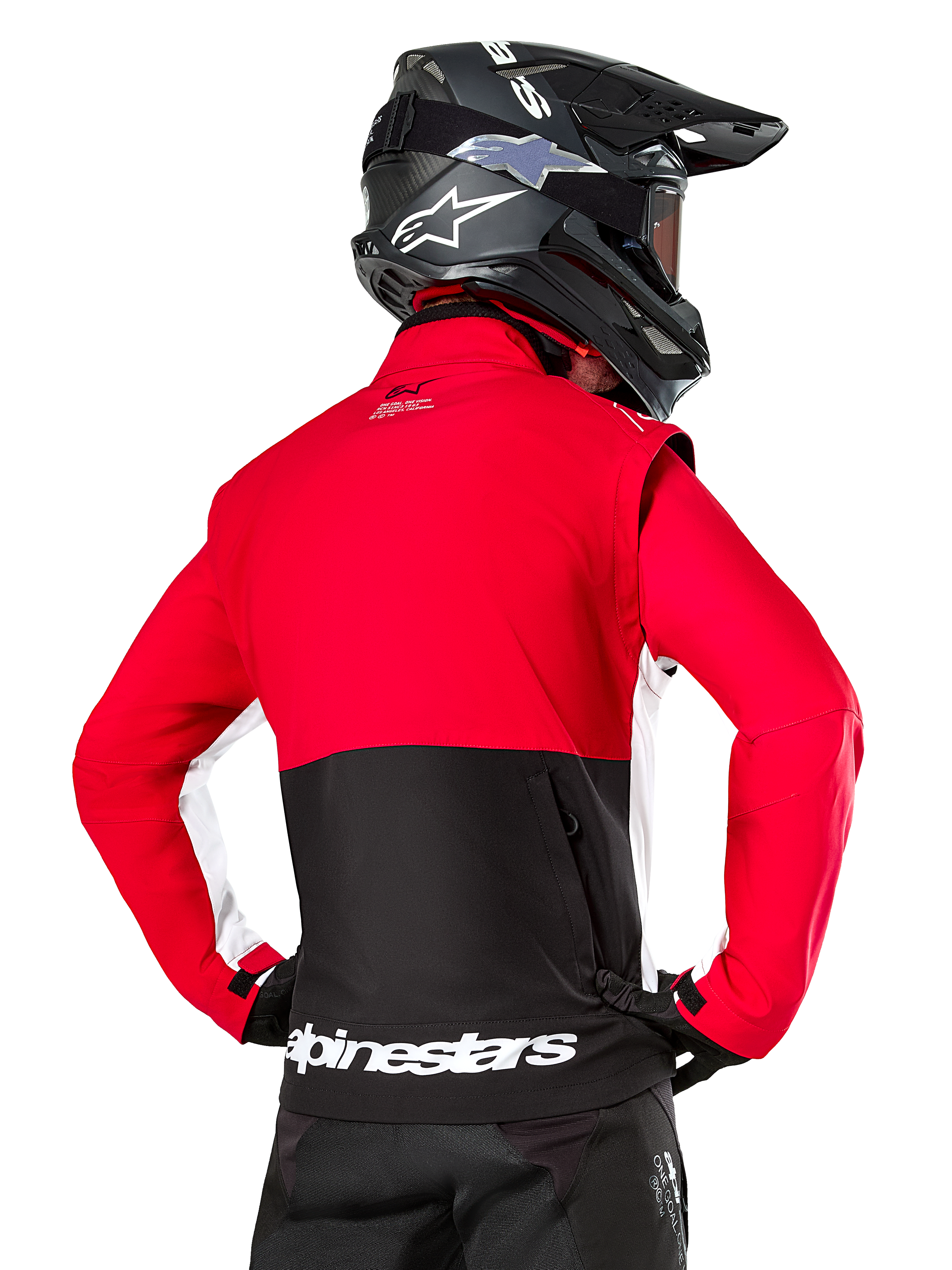 Alpinestars Lite-Dura Softshell Jacket, negro, rojo brillante y blanco, vista trasera en un piloto de motocross, parte superior del cuerpo y mangas en rojo con panel inferior trasero negro, bolsillo de almacenamiento trasero con cremallera, logotipo blanco de Alpinestars en el dobladillo inferior, usada con casco y pantalones negros