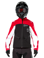 Chaqueta Softshell Alpinestars Lite-Dura en negro, rojo brillante y blanco, usada por un piloto de motocross con casco negro y gafas de lentes rojas, con paneles blancos en las mangas, logotipo de Alpinestars en el pecho y diseño deportivo para todoterreno