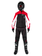 Piloto de motocross con la chaqueta softshell Alpinestars Lite-Dura en negro, rojo brillante y blanco, combinada con pantalones off-road negros, botas negras y blancas, y casco negro con gafas; equipamiento completo para competiciones de enduro