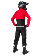 Piloto de motocross visto desde atrás con la Chaqueta Alpinestars Lite-Dura Softshell, negro, rojo brillante y blanco, con un panel superior rojo y sección inferior negra con logotipo blanco, combinado con pantalones negros, casco negro y botas negras, conjunto de enduro coordinado para conducción off-road