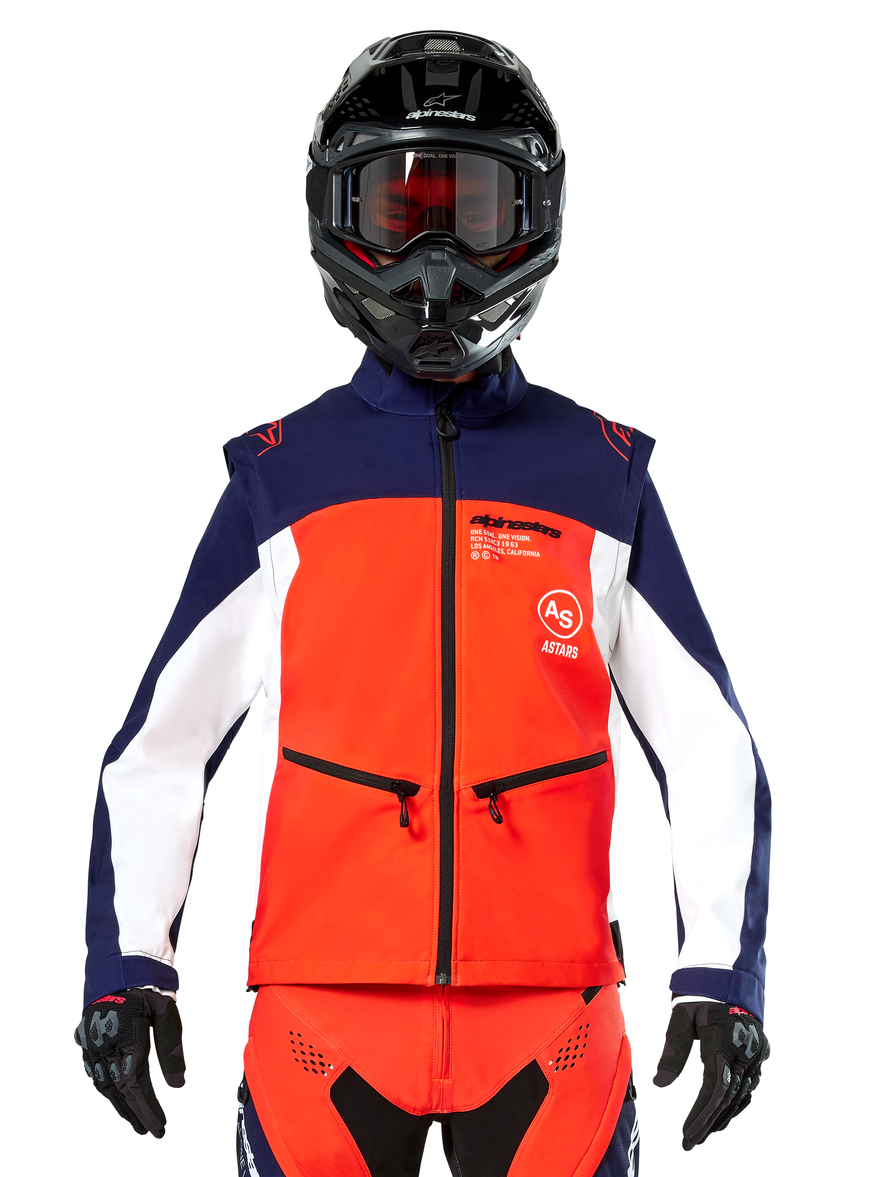 Chaqueta Softshell Alpinestars Lite-Dura en azul marino, naranja intenso y blanco, vista frontal de un piloto con casco negro y gafas, con diseño técnico de bloques de color, bolsillos con cremallera y logotipos de Alpinestars, equipamiento versátil para enduro y conducción off-road