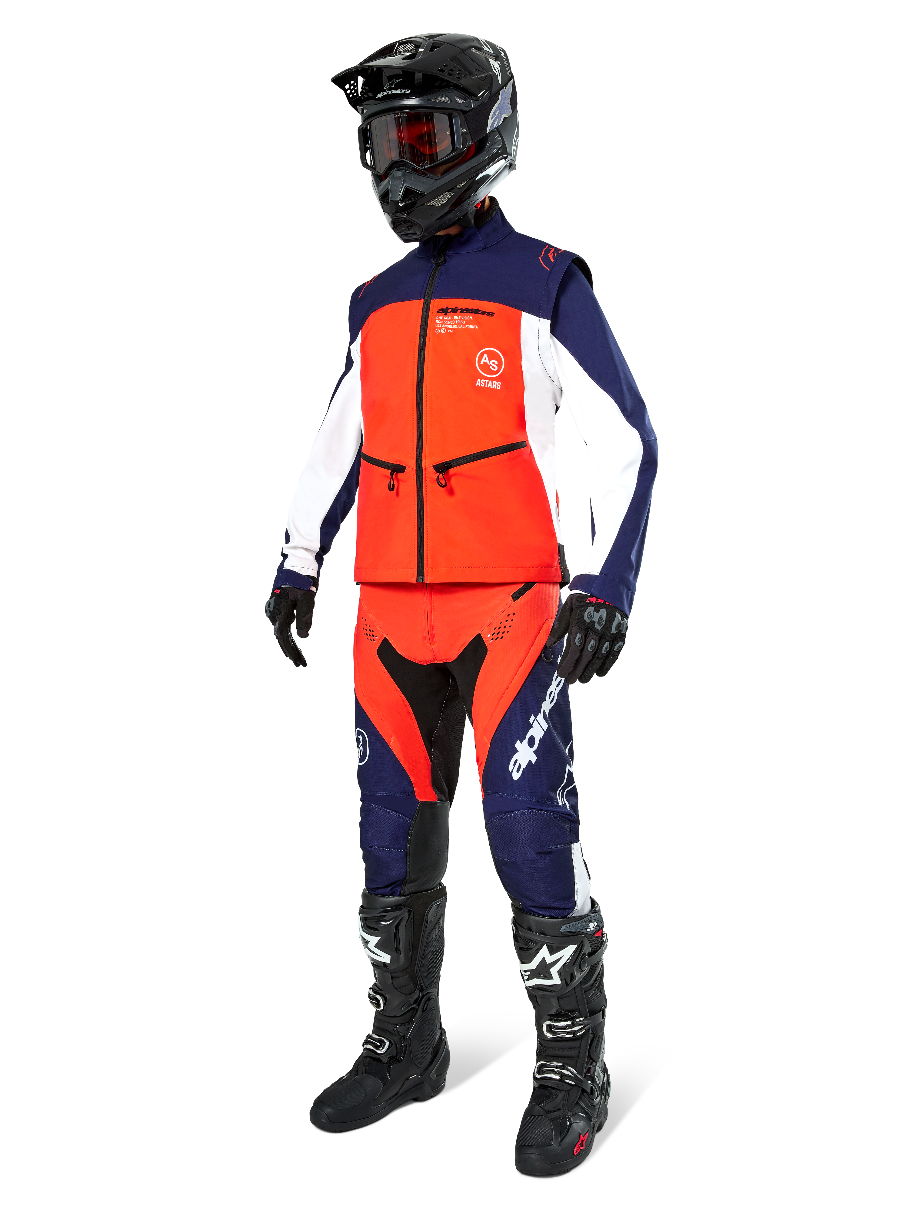 Piloto de motocross con la chaqueta Alpinestars Lite-Dura Softshell en azul marino, naranja intenso y blanco, pantalones de off-road a juego, casco negro con gafas y botas de carreras negras, conjunto completo de equipamiento de enduro
