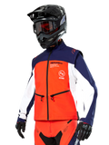 Chaqueta Softshell Alpinestars Lite-Dura en azul marino, naranja intenso y blanco, equipamiento de motocross, combinada con casco y gafas negras, guantes protectores y pantalones de carreras a juego