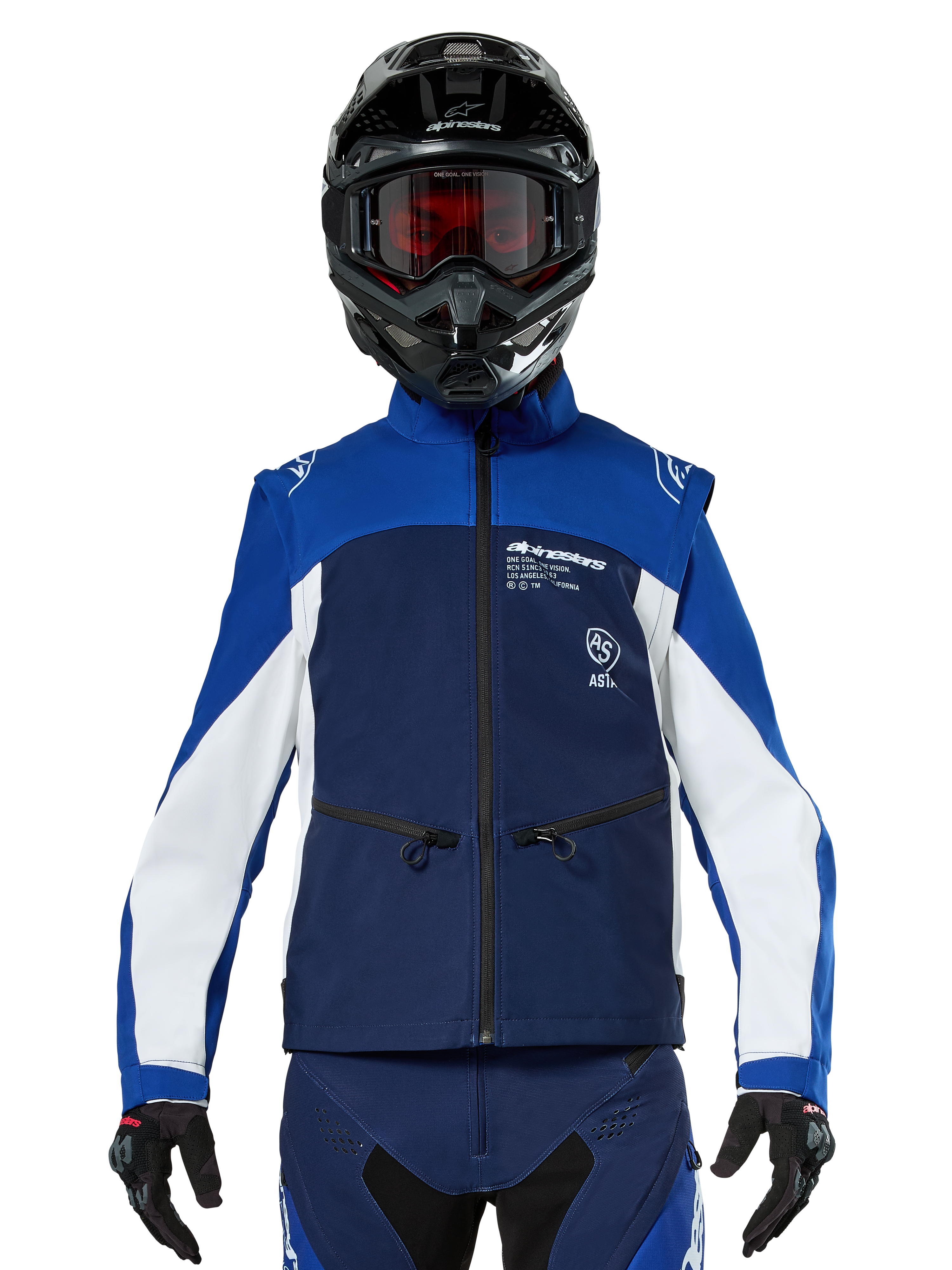 Piloto de motocross con la chaqueta Alpinestars Lite-Dura Softshell en azul marino, azul brillante y blanco, vista frontal, combinada con un casco negro y gafas con lentes rojas, con un diseño técnico cortavientos con bolsillos con cremallera y detalles en blanco para conducción de enduro off-road