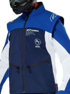 Chaqueta Softshell Alpinestars Lite-Dura, chaqueta de motocross y enduro, azul marino, azul brillante y blanco, con logotipos de Alpinestars en blanco en el pecho y bolsillos con cremallera, usada con un casco negro, construcción de softshell duradera con mangas desmontables para conducción off-road