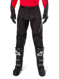 Pantalones Alpinestars Pro-Dura, pantalones de enduro en color negro y magnet, combinados con un jersey rojo de manga larga y botas de motocross negras, con logotipos grises de Alpinestars y una construcción de ripstop resistente para conducción off-road.