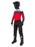 Pantalones Alpinestars Pro-Dura en negro magnet blanco, usados por un piloto con un jersey a juego en rojo, negro y blanco, casco negro y botas off-road negras, conjunto completo de equipamiento profesional de enduro para rendimiento off-road.