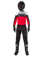 Piloto de motocross con pantalones Alpinestars Pro-Dura en color negro y magnet, combinados con un jersey rojo, blanco y negro, casco negro y botas negras, kit completo de equipamiento para carreras off-road, diseño duradero y ligero para conducción de enduro