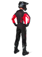 Piloto de motocross visto desde atrás vistiendo pantalones Alpinestars Pro-Dura en color Black Magnet White, combinados con un jersey rojo y negro y botas negras, conjunto coordinado de equipamiento off-road para enduro