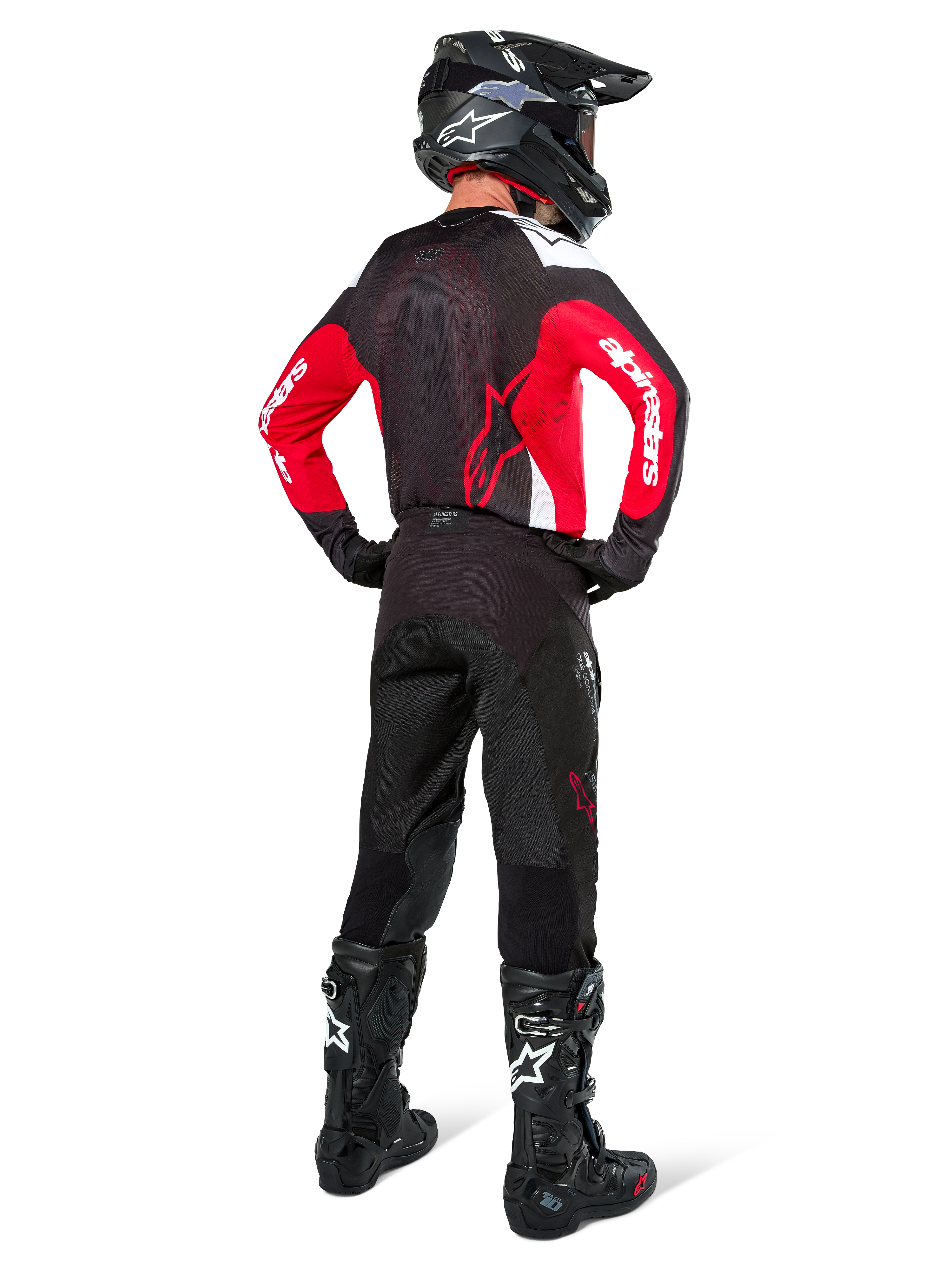 Piloto de motocross visto desde atrás vistiendo pantalones Alpinestars Pro-Dura en color Black Magnet White, combinados con un jersey rojo y negro y botas negras, conjunto coordinado de equipamiento off-road para enduro