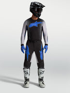 Pantalones Alpinestars Supertech Hiten AFD, equipo de motocross negro y azul, con jersey a juego y botas de carreras blancas.