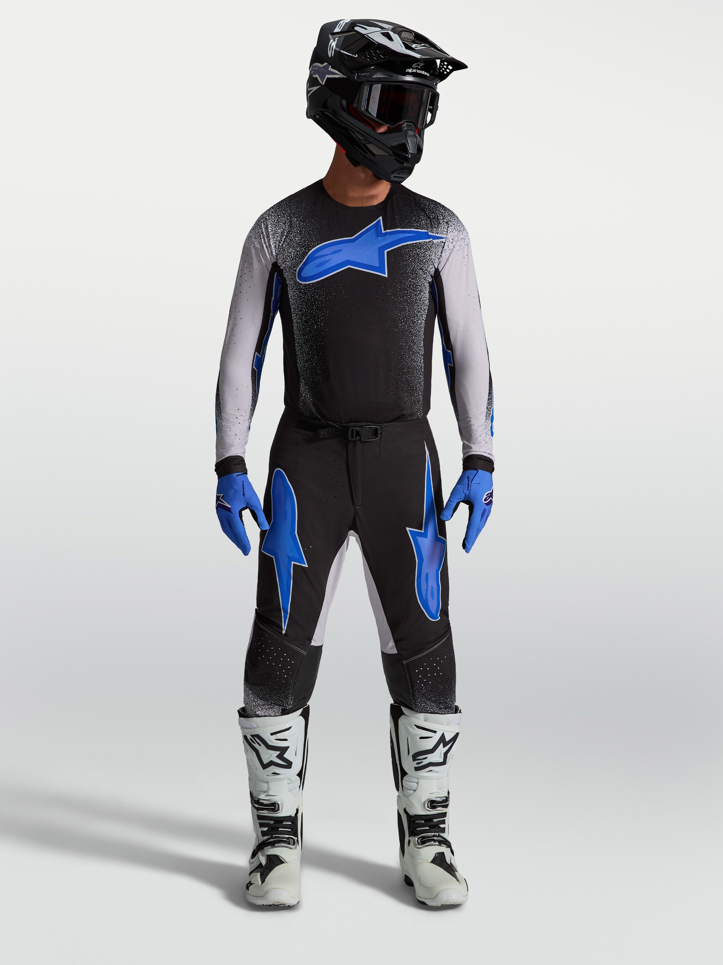 Pantalones Alpinestars Supertech Hiten AFD, equipo de motocross negro y azul, con jersey a juego y botas de carreras blancas.