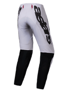 Alpinestars Supertech Maker 2025, pantalones de motocross, plata y negro, vista trasera con logotipo Alpinestars grande en negro en el lateral, paneles inferiores de las piernas en negro y pequeños logotipos de estrellas rojas en la cintura, diseñados para un rendimiento profesional todoterreno.