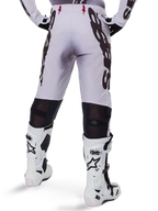 Alpinestars 2025 Supertech Maker Pants, pantalones de motocross, plateado y negro, vista trasera con grandes logotipos negros en los muslos y zonas de malla transpirable detrás de las rodillas, usados con botas Alpinestars blancas