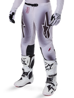 Pantalones Alpinestars Supertech Maker 2025, pantalones de motocross, en color plata y negro, con logotipos de estrellas grandes y letras rojas, mostrados con botas y guantes blancos a juego