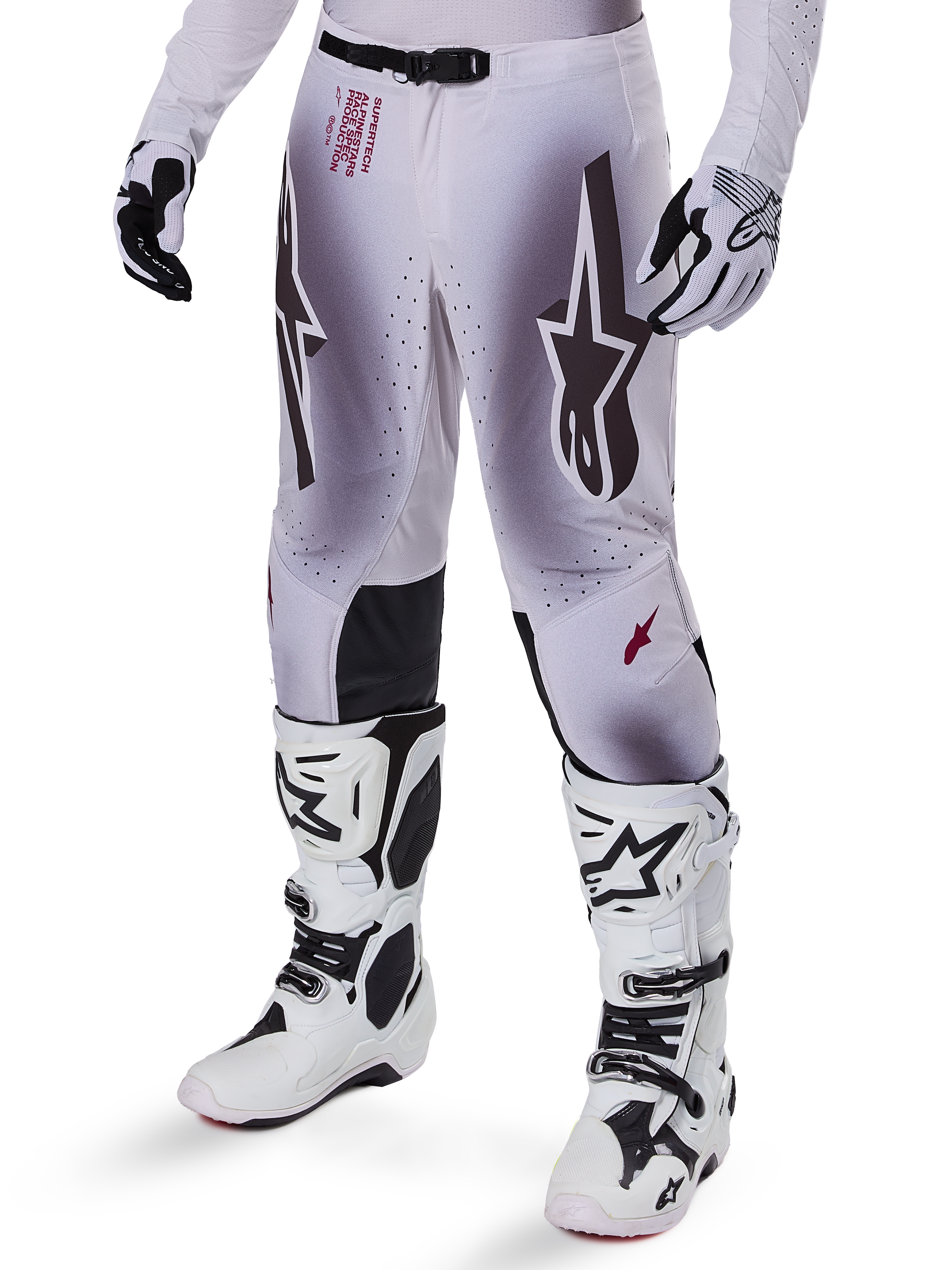 Pantalones Alpinestars Supertech Maker 2025, pantalones de motocross, en color plata y negro, con logotipos de estrellas grandes y letras rojas, mostrados con botas y guantes blancos a juego