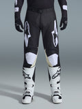 Alpinestars 2026 Racer Air Riway Pants, pantalones de motocross, negro y blanco, con llamativos logotipos blancos de Alpinestars en los muslos y paneles de las rodillas, combinados con botas de motocross blancas y negras y guantes negros, diseño atlético de ajuste de carrera para conducción off-road